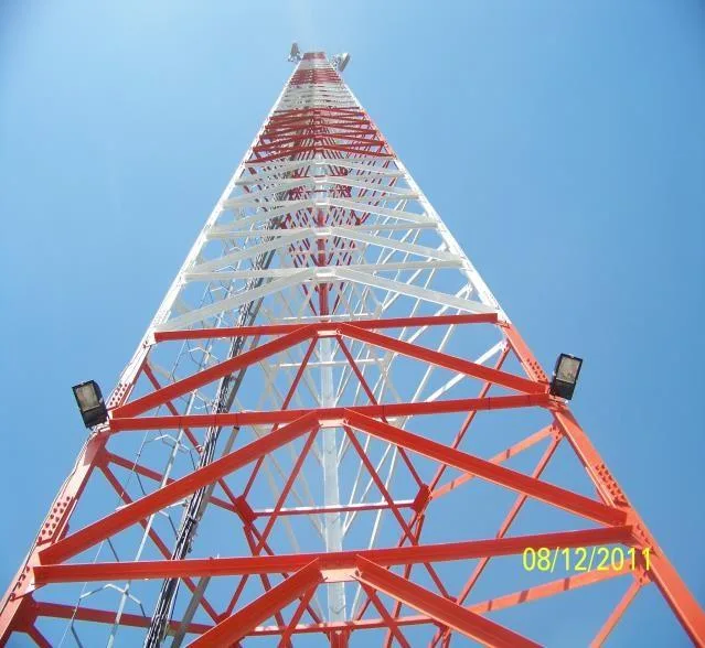 Looking up a red and white lattice telecoms mast built by our team, with floodlights on the lower section